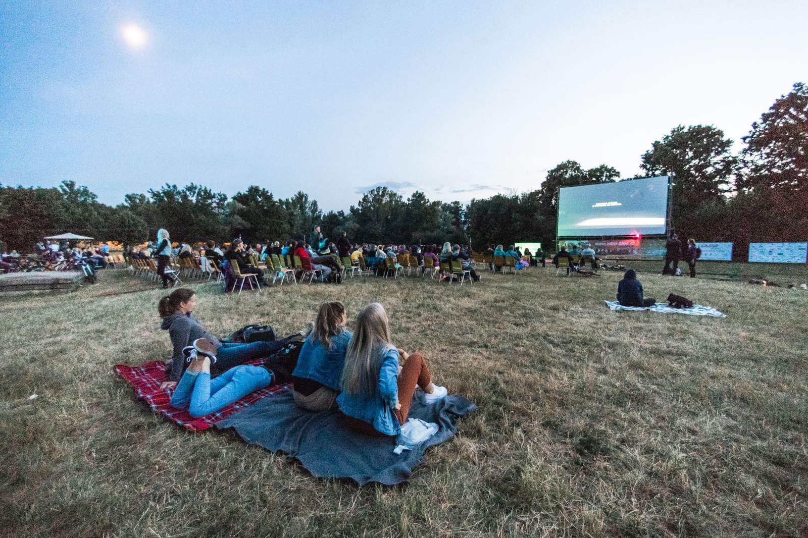 Families seated on blankets and lawn chairs watching an outdoor movie screen at Heritage Park in Flower Mound