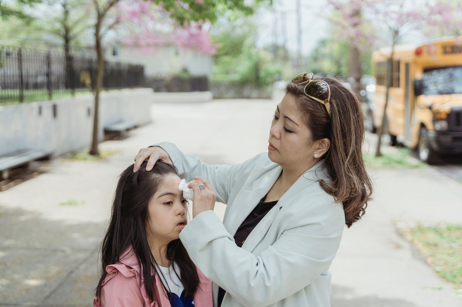 A parent and young child waiting at a school bus stop on a residential street on a weekday morning